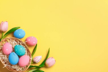 Paskalya tebrik kartı davetiyesi. Sepette çok renkli boyanmış yumurtalar, sarı arka planda pembe laleler.