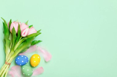 Yeşil arkaplanda paskalya yumurtaları ve pembe laleler. Düz yatay kopyalama alanı olan üst görünüm.