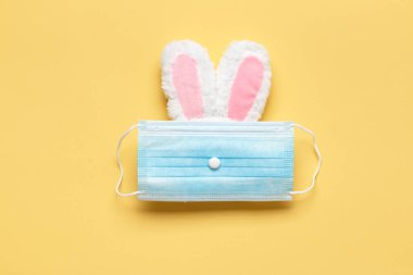 Paskalya ve karantina. Sarı arka planda koruyucu tıbbi maskeli bir tavşan..