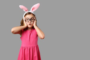 Paskalya tavşanı kulaklı ve gözlüklü küçük bir kız. Gri arkaplanda bir çocuğun portresi.