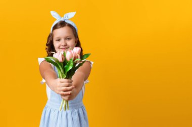 Bahar ve Anneler Günü konsepti. Sarı arka planda sevimli, mutlu küçük bir kız. Çocuk elinde bir buket lale tutuyor..