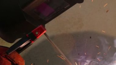 Koruyucu maskeli bir kaynakçı metal kaynaklama yapıyor. Yakın çekim gerçek zamanlı duman flaşı.