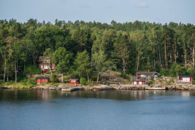 Kayalık sahildeki kırmızı evler ağaçlarla çevrili.