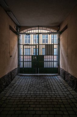 Metal kapılı ve bina manzaralı karanlık dar bir geçit.