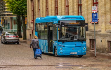 Göteborg, İsveç - 10 Ekim 2024: Alışveriş arabasıyla küçük mavi bir otobüse doğru yürüyen yaşlı kadın