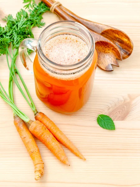 Glasses of carrot juice with carrot roots on wooden background.G