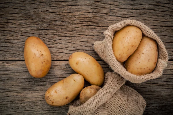 Fresh organic potatoes in hemp sake bags on rustic wooden backgr — Stock Photo, Image