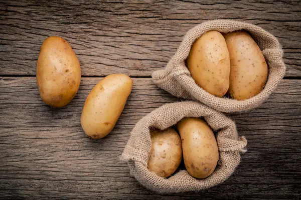 Fresh organic potatoes in hemp sake bag on rustic wooden backgro — Stock Photo, Image