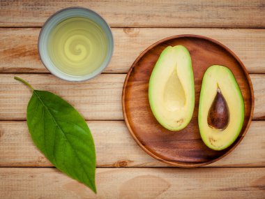 Fresh avocado with avocado leaves and oil on wooden background.  clipart