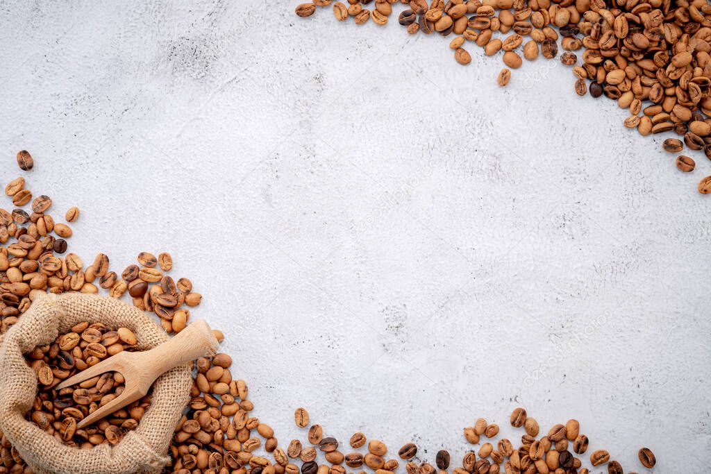 Roasted coffee beans with scoops setup on white concrete background.