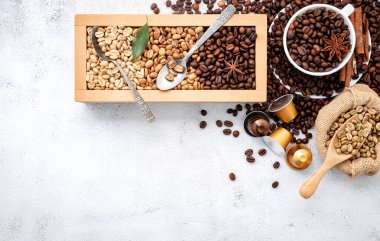 Kahverengi ve yeşil kafeinsiz kavrulmuş ve kavrulmuş kahve çekirdekleri ahşap kutuda, kepçeler beyaz beton arka planda..