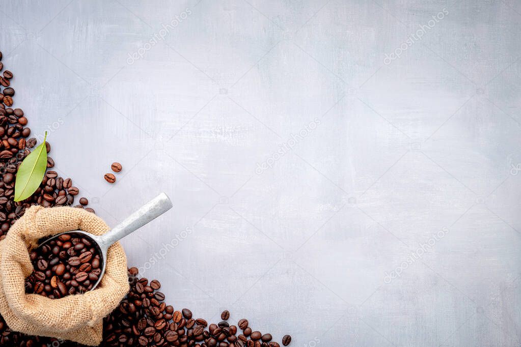 Dark roasted coffee beans in hemp sack bags with scoops setup on white concrete background.
