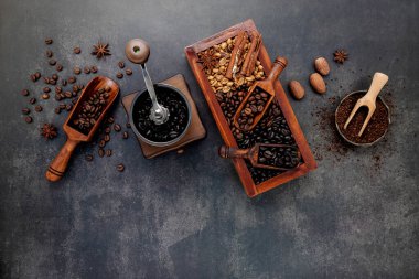 Ahşap kutuda, koyu taştan arka planda manuel kahve öğütücüsüyle hazırlanmış çeşitli kahve çekirdekleri..