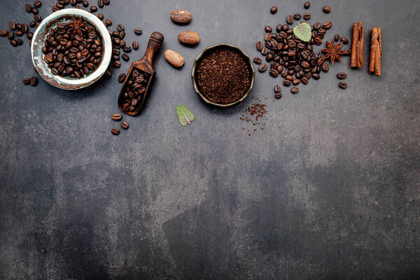 Roasted coffee beans with coffee powder and flavourful ingredients for make tasty coffee setup on dark stone background.