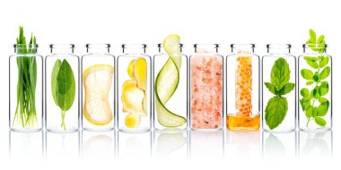 Doğal malzeme içeren ev yapımı cilt bakımı buğday, adaçayı, limon, zencefil, salatalık, himalaya tuzu, bal peteği, nane ve moringa yaprakları beyaz arka planda izole edilmiş cam şişelerde..