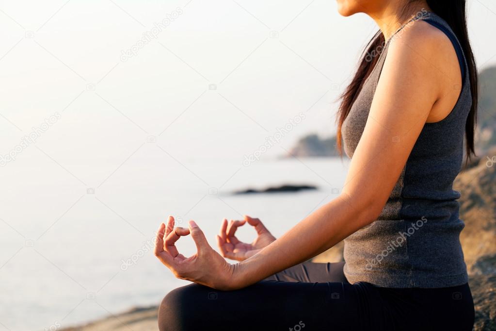 The woman meditating in a yoga pose on the tropical beach.