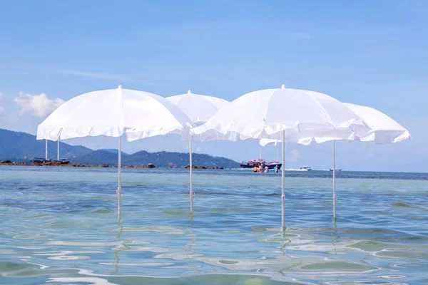 Guarda-chuva branco na praia tropical de verão com barco à vela . — Fotografia de Stock