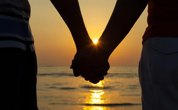 Silhuetas casais de mãos dadas no pôr do sol . — Fotografia de Stock