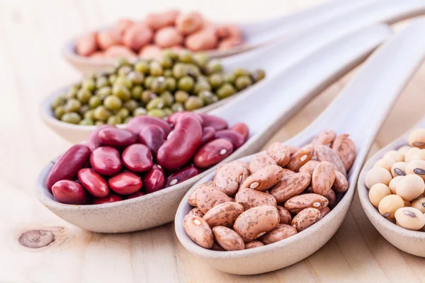 Assortment of beans and lentils in wooden spoon on wooden backgr