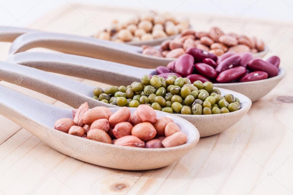 Assortment of beans and lentils in wooden spoon on wooden backgr