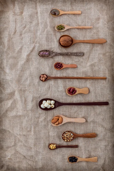 Various beans and nuts in the wooden spoon on brown cloth — Zdjęcie stockowe