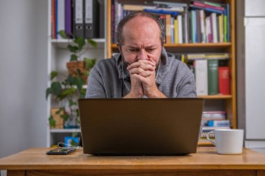 Ev ofisinden bilgisayarda çalışan bir adam klasik masanın arkasında, kulaklıklı, çevrimiçi görüşmeleri dinleyen bir adam.