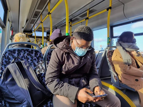 Berlin Almanya Kasım 2020, maskeli bir yolcu ve elinde bir akıllı telefon bir otobüste oturuyor.