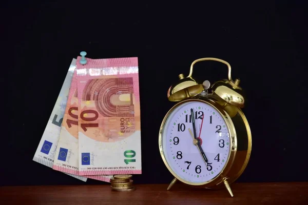 money and alarm clock on black background