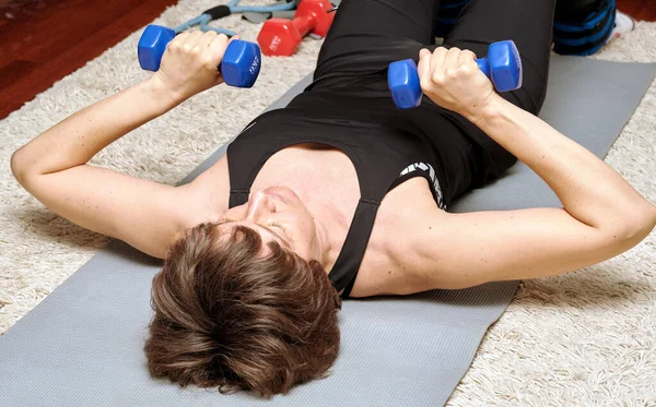home fitness - woman with dumbbells doing gymnastic exercises lying on the floor