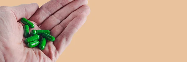 Kırmızı tabletler bir adamın buruşuk avuçlarında, yeşil arka planda izole edilmiş görüntüler.