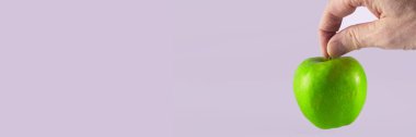 yeşil elma bir adamın parmaklarını kuyruğundan tut, soluk pembe arka plan, mesaj için yer