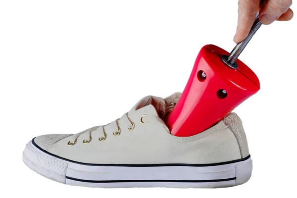 Ayakkabı germek için kullanılan kırmızı renk aygıtı beyaz arka planda beyaz bir spor ayakkabısına takılır.