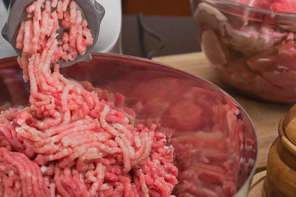Kıyma ızgaradan geçer ve paslanmaz çelik bir kaseye düşer. Evde hamburgerler için malzemeler.