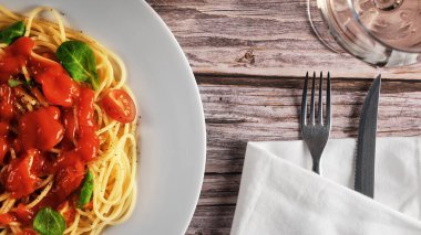 Makarnalı büyük tabak, çatal ve bıçaklı peçete, ahşap bir masada beyaz şarap kadehi, üst manzara, köy tarzı.