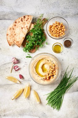 Nohutlu taze humus, zeytinyağı, açık gri masada cam kasede kırmızı biber, malzemeler serbestçe dizilmiş. Küçük bir doğrama tahtasının üzerinde humus ile birlikte taze maydanoz.