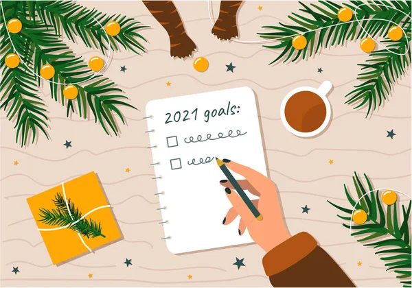 Yeni yıl için yapılacaklar listesi ve hedefler. Bir kadının gelecek için el yazısı planları Noel dalları, Noel süslemeleri ve oyuncak çalan kedi patileriyle çevrili..