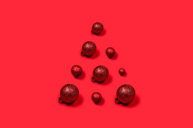 Parlak arkaplanda üçgen şeklinde dizilmiş kırmızı Noel toplarının cildi.