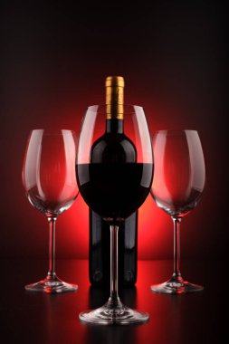 Şarap şişeleri ve kırmızı ve siyah siluetli dolu bardaklar.