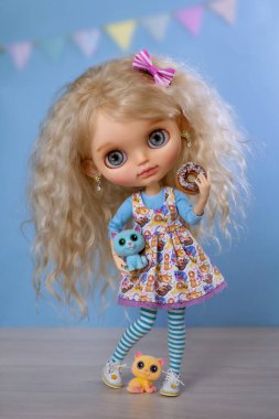 Sarışın, kıvırcık saçlı, mavi gözlü bir bebek güzel elbiseli bir kız elinde lezzetli bir çörek ve yanında iki kedi var.