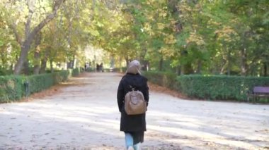 Asyalı genç bir kadın gölgeli ağaçlar ve düşmüş yapraklarla bir bahçenin ortasında tek başına yürüdü.