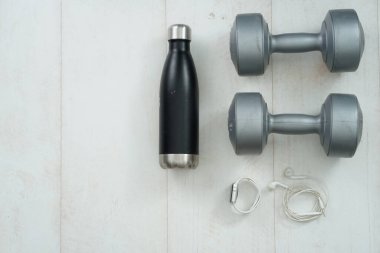 Spor aletleri, ayakkabılar, su, dambıllar, kulaklık ve telefon ahşap zemin üzerinde düz çekim