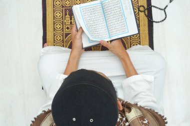 Kutsal Kur 'an ve ibadet halılarıyla caminin içinde dua eden dindar Müslüman adam.