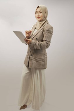 Güzel, tesettürlü, tesettürlü bir kadın tablet bilgisayara sarılmış ve beyaz duvar arkasına izole edilmiş, stüdyo portresi çizmiş. İnsanlar dini yaşam tarzı konsepti. Kopyalama alanı oluştur