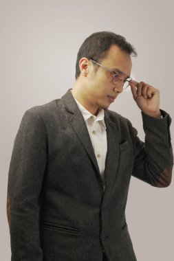 Gözlüklü ve koyu renk takım elbiseli kendine güvenen genç adam gri arka planda izole edilmiş..