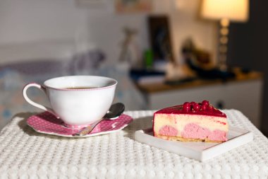 Kırmızı böğürtlen ve bir fincan çayla vanilyalı kremalı pasta. Ev arka planında sıcak bir kahve. Çay saati konsepti.