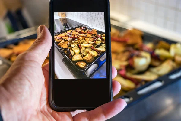 Mannelijke hand nam een foto van geroosterde groenten op ovenschaal thuis — Stockfoto