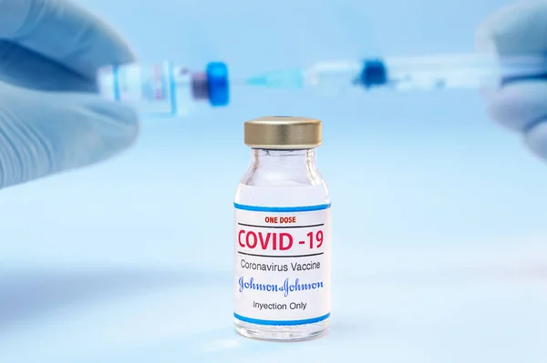 Flacone da una dose di vaccino coronavirus Jhonson e Jhonson e mani di medico con sfondo siringa. — Foto Stock