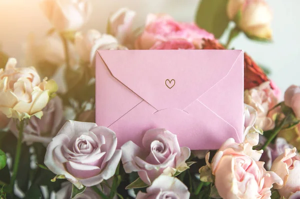 pink notepad with greeting card in bright beautiful bouquet of colorful roses, concept of congratulations on the holiday