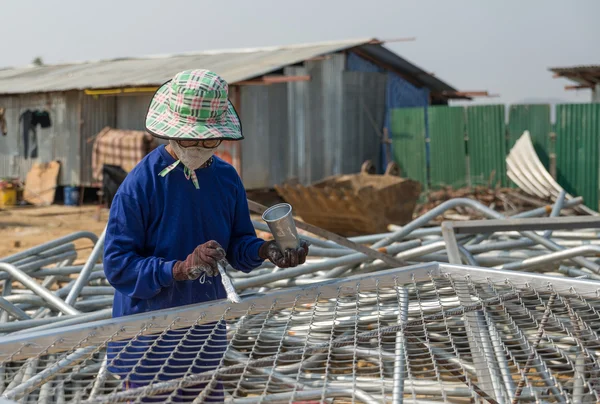 Een vrouw schildert draad metalen hek in zilveren kleur — Stockfoto