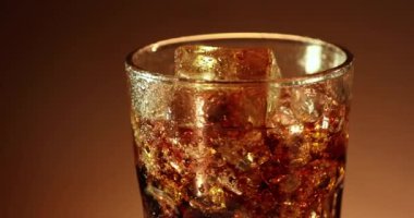 Buzlu kola bardağı yavaşça yakın çekimde dönüyor. Kahverengi arka planda dönen soğuk soda içeceği. 4K video görüntüleri